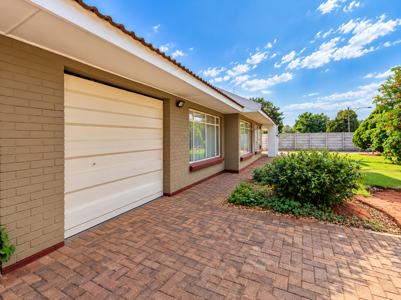 A well-maintained front exterior featuring a brick facade, paved driveway, and a secure garage door, complemented by neat landscaping and a clear blue sky.