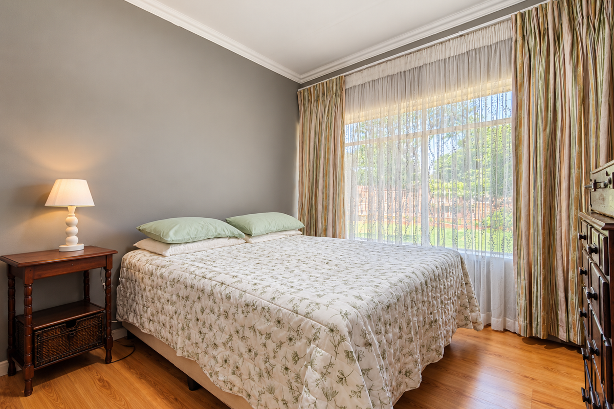A well-maintained bedroom featuring warm laminate flooring, crown molding, and a large window with natural light.