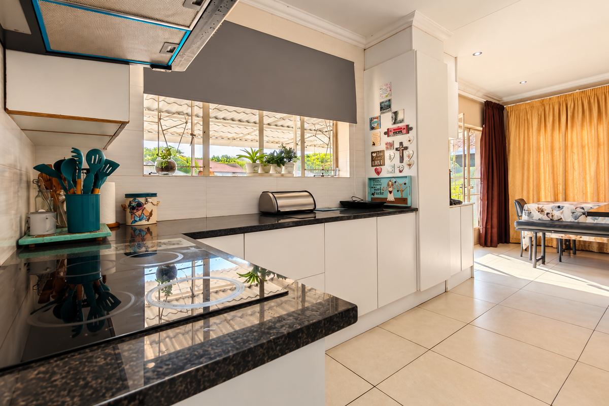 Modern kitchen featuring granite countertops, built-in electric hob, stainless steel extractor fan, and tiled flooring, seamlessly flowing into the adjacent dining area.