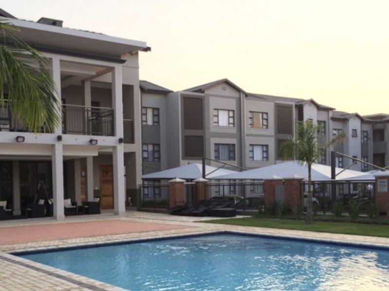 A well-maintained apartment complex featuring a communal swimming pool, paved deck area, and covered patio spaces for residents.