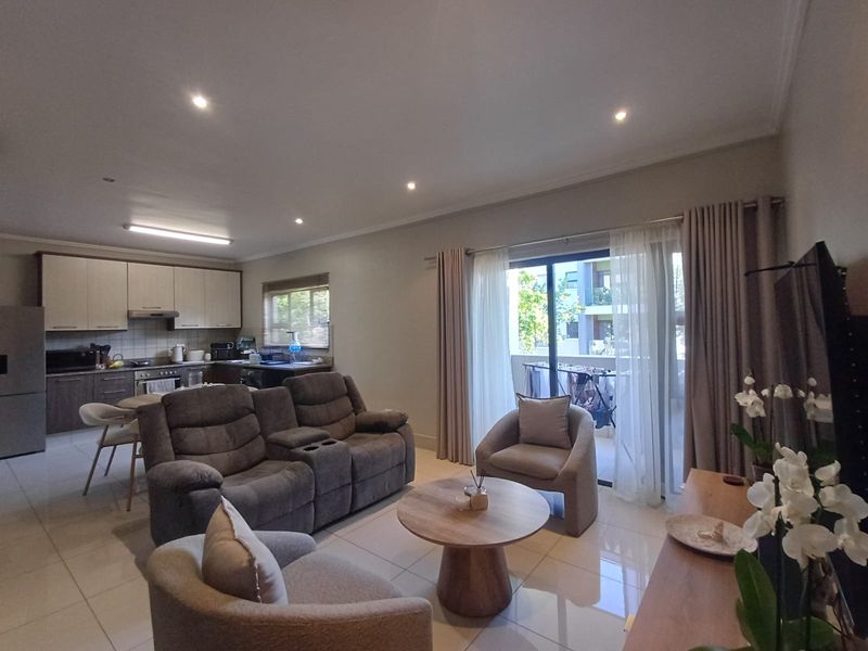 An open-plan living and kitchen area featuring modern cabinetry, tiled floors, and a sliding glass door leading to a private balcony.