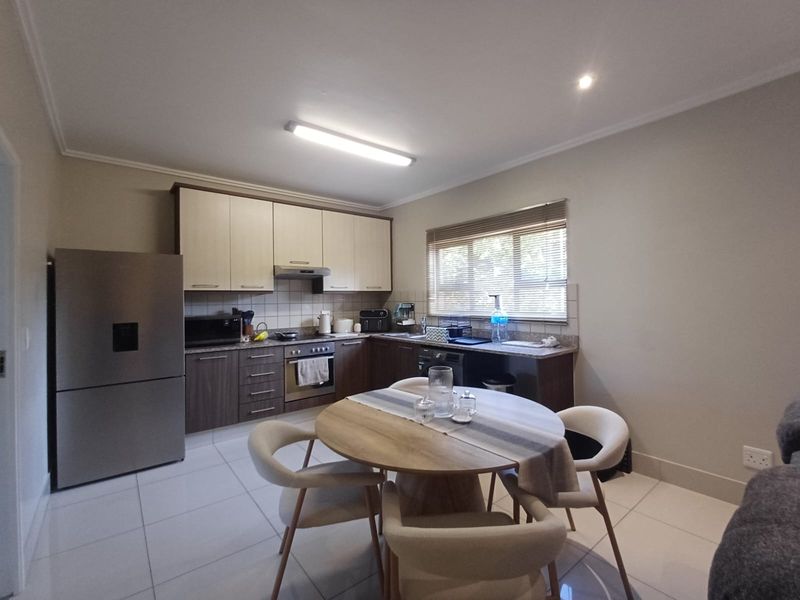 Open-plan kitchen and dining area featuring modern two-tone cabinetry, tiled flooring, and integrated appliances, creating a functional and cohesive living space.