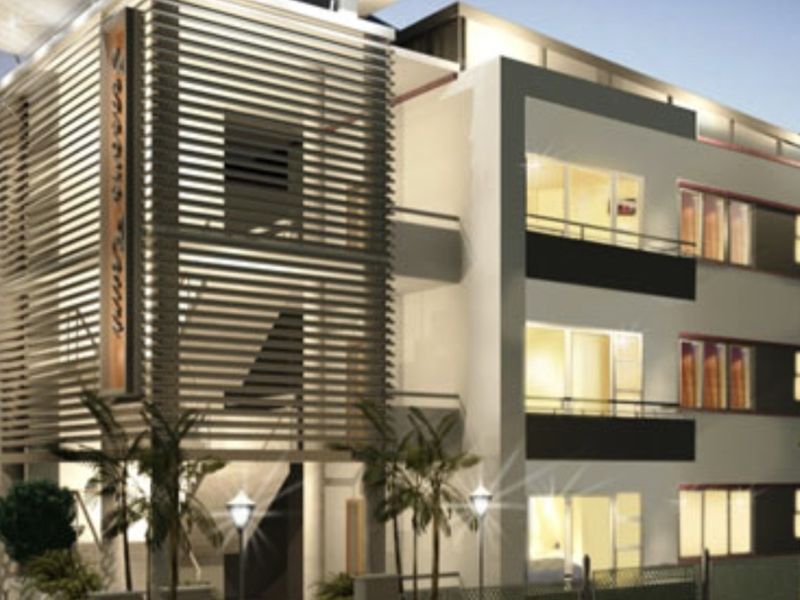 Modern multi-story apartment building exterior featuring a distinctive louvred facade screen, private balconies, and integrated exterior lighting.