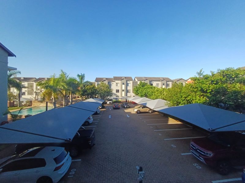 An elevated view of the apartment complex parking area featuring covered parking bays, paved driveway, and communal swimming pool access.