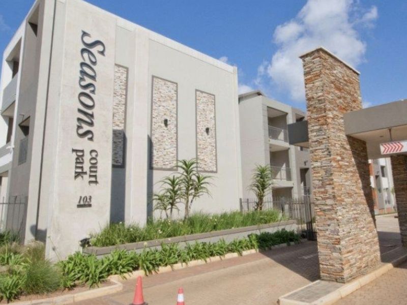 Front elevation of Seasons Court apartment complex featuring modern stone cladding, paved driveway access, and balcony structures.