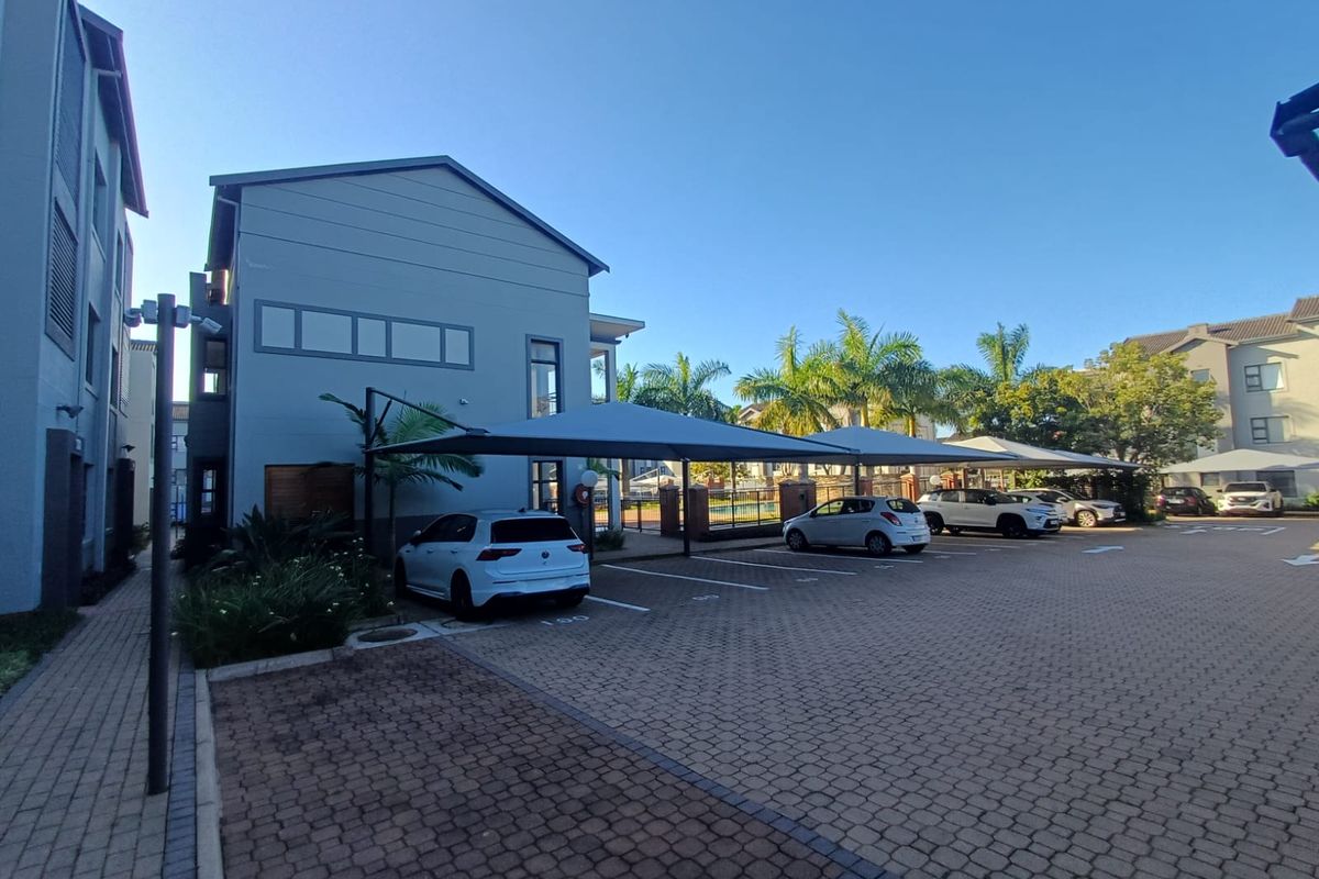 Exterior view of the apartment complex parking area featuring paved driveway and covered shade cloth parking bays.