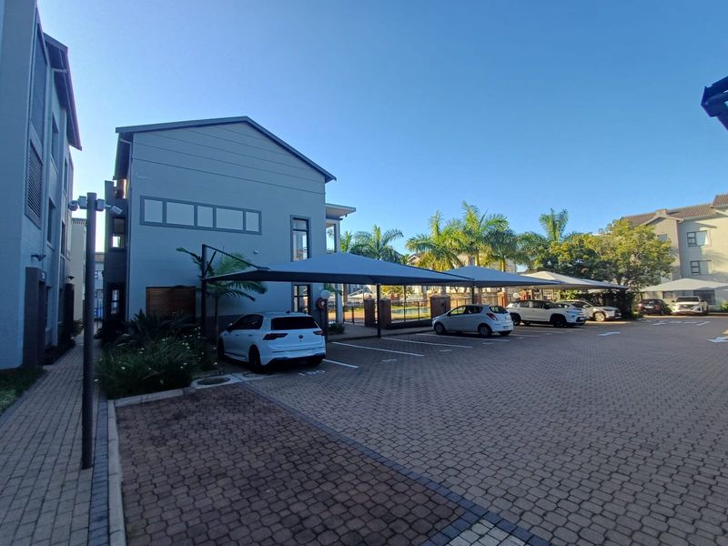 Exterior view of the apartment complex parking area featuring paved driveway and covered shade cloth parking bays.