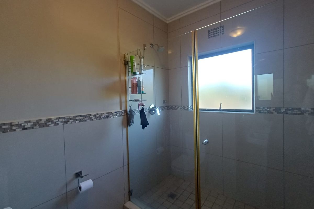 A functional bathroom featuring a glass-enclosed shower with tiled walls, a mosaic accent border, and a frosted window for natural light and privacy.
