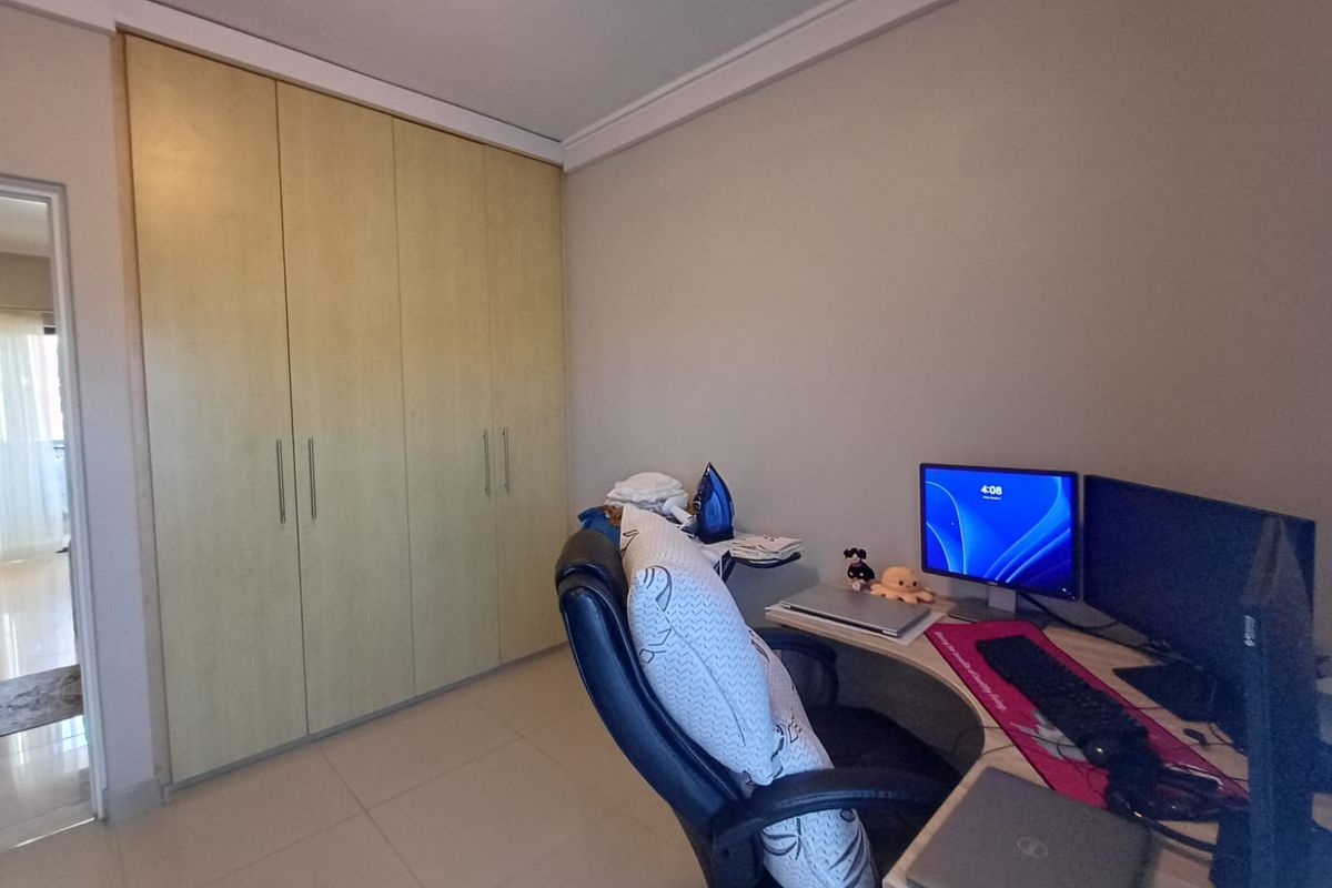 A functional bedroom featuring light-toned built-in wardrobes, neutral tiled flooring, and decorative cove cornicing, currently utilized as a home office space.