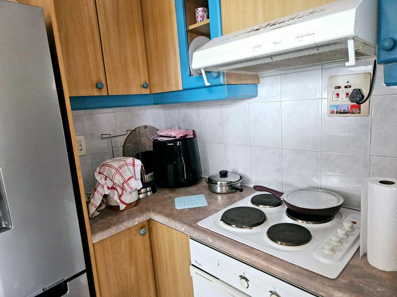Compact kitchen featuring laminate cabinetry, tiled backsplash, and integrated electric hob with extractor fan, offering a functional layout for efficient meal preparation.