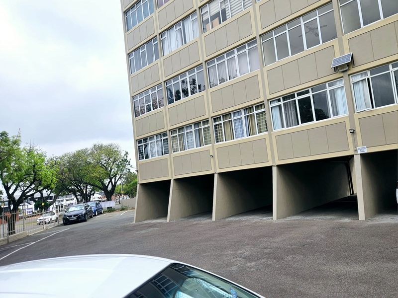 Exterior view of a multi-story apartment building featuring a facade with aluminum windows and ground-level covered parking bays.