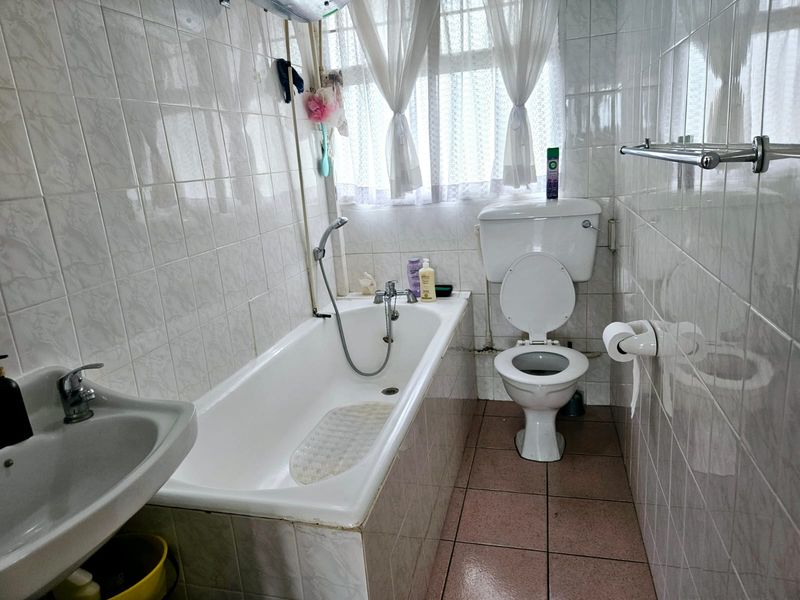 A functional bathroom featuring a bathtub, pedestal basin, and toilet with fully tiled walls and flooring, offering potential for modernization.