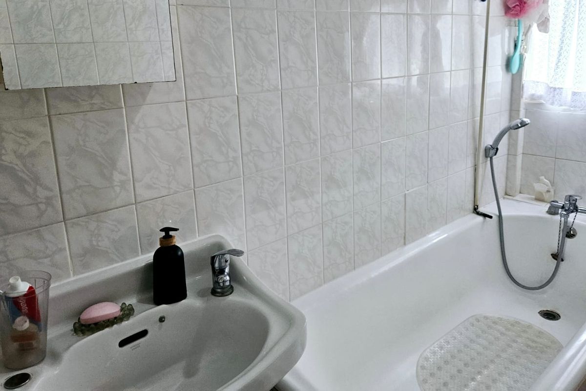 A functional bathroom featuring a pedestal basin, bathtub with shower attachment, and classic ceramic wall tiling.