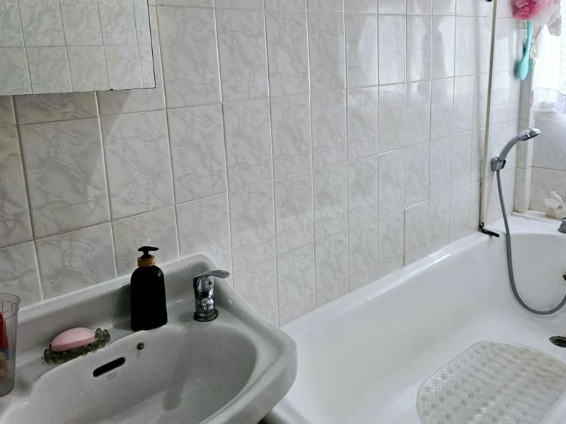 A functional bathroom featuring a pedestal basin, bathtub with shower attachment, and classic ceramic wall tiling.