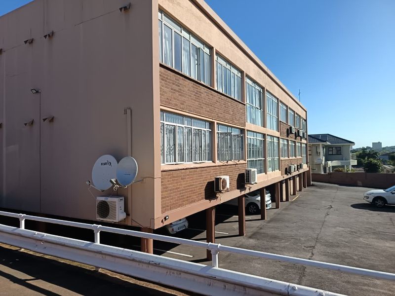 Exterior view of a multi-story apartment building featuring brick cladding, under-building parking, and external air conditioning units.