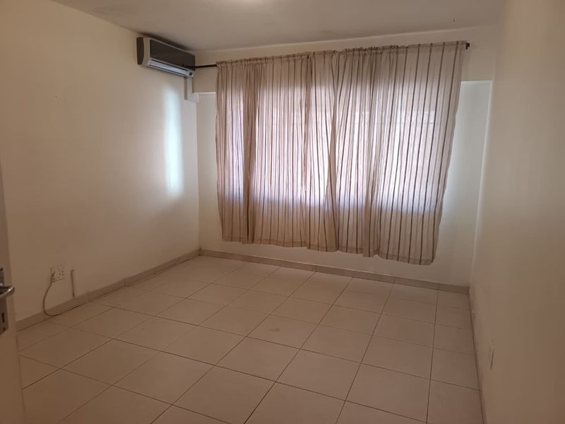 An empty bedroom featuring tiled flooring and a wall-mounted air conditioning unit, providing a neutral canvas for personalization.