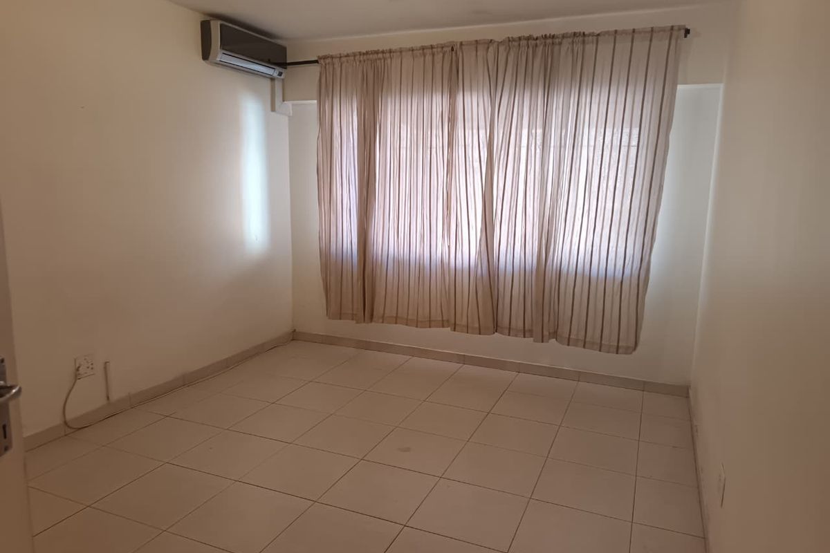 An empty bedroom featuring tiled flooring and a wall-mounted air conditioning unit, providing a neutral canvas for personalization.