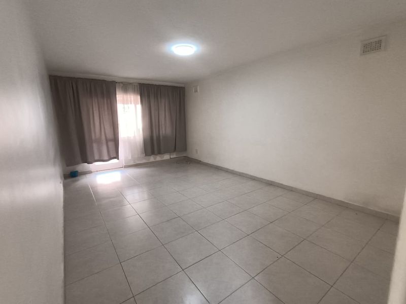 An empty, neutrally finished living room featuring tiled flooring and natural light access through a window with curtain tracks.