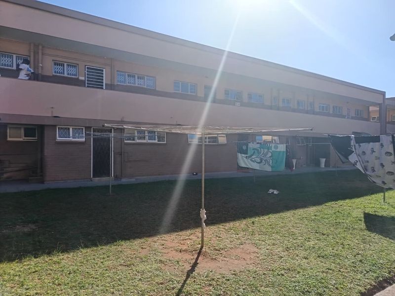Rear view of a multi-story flat complex featuring a communal lawn area and security-fitted windows.