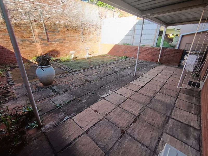 A covered outdoor patio area featuring paved flooring and brick boundary walls, offering a blank canvas for potential landscaping or outdoor living improvements.