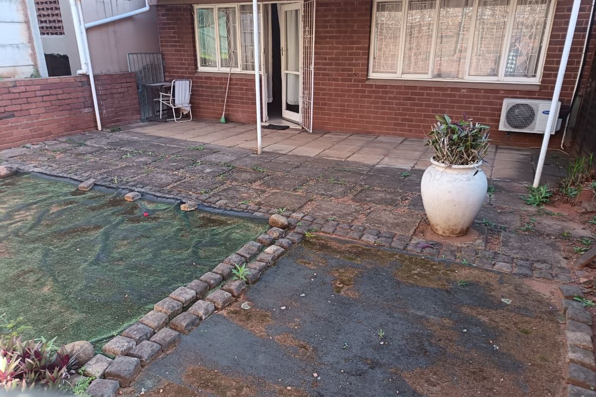 Rear exterior view of the flat featuring a paved patio area, brick facade, and covered outdoor space with an installed air conditioning unit.