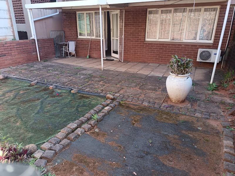 Rear exterior view of the flat featuring a paved patio area, brick facade, and covered outdoor space with an installed air conditioning unit.