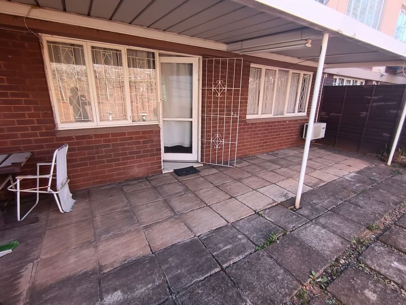 A covered patio area featuring brick exterior walls, security gates, and paved flooring, providing a functional outdoor space for the flat.
