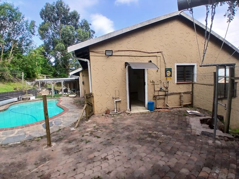Rear exterior view of the cottage featuring a swimming pool, paved patio area, and external utility connections.