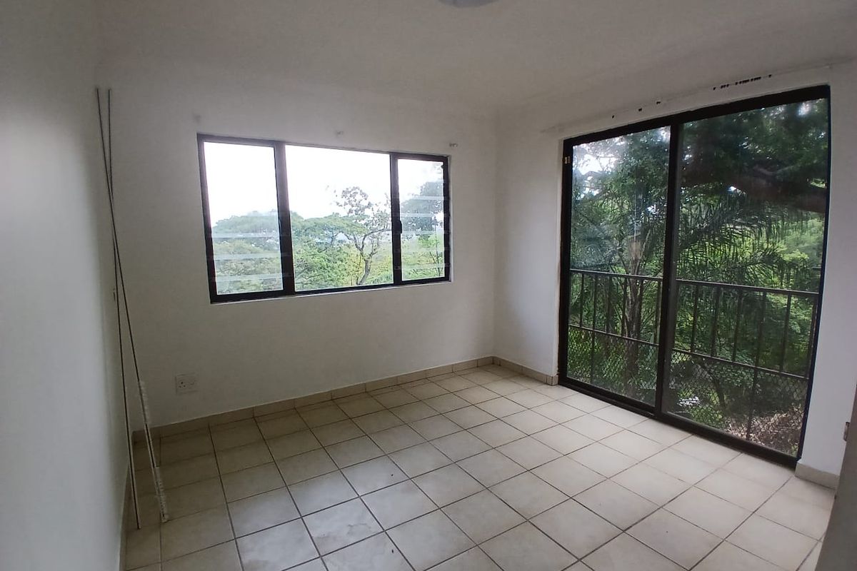 An empty bedroom featuring tiled flooring, large windows, and a sliding glass door leading to an outdoor area with a security gate.