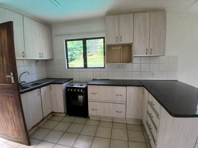 A functional kitchen featuring laminate cabinetry, black countertops, a freestanding stove, and tiled flooring, offering a blank canvas for potential cosmetic updates.