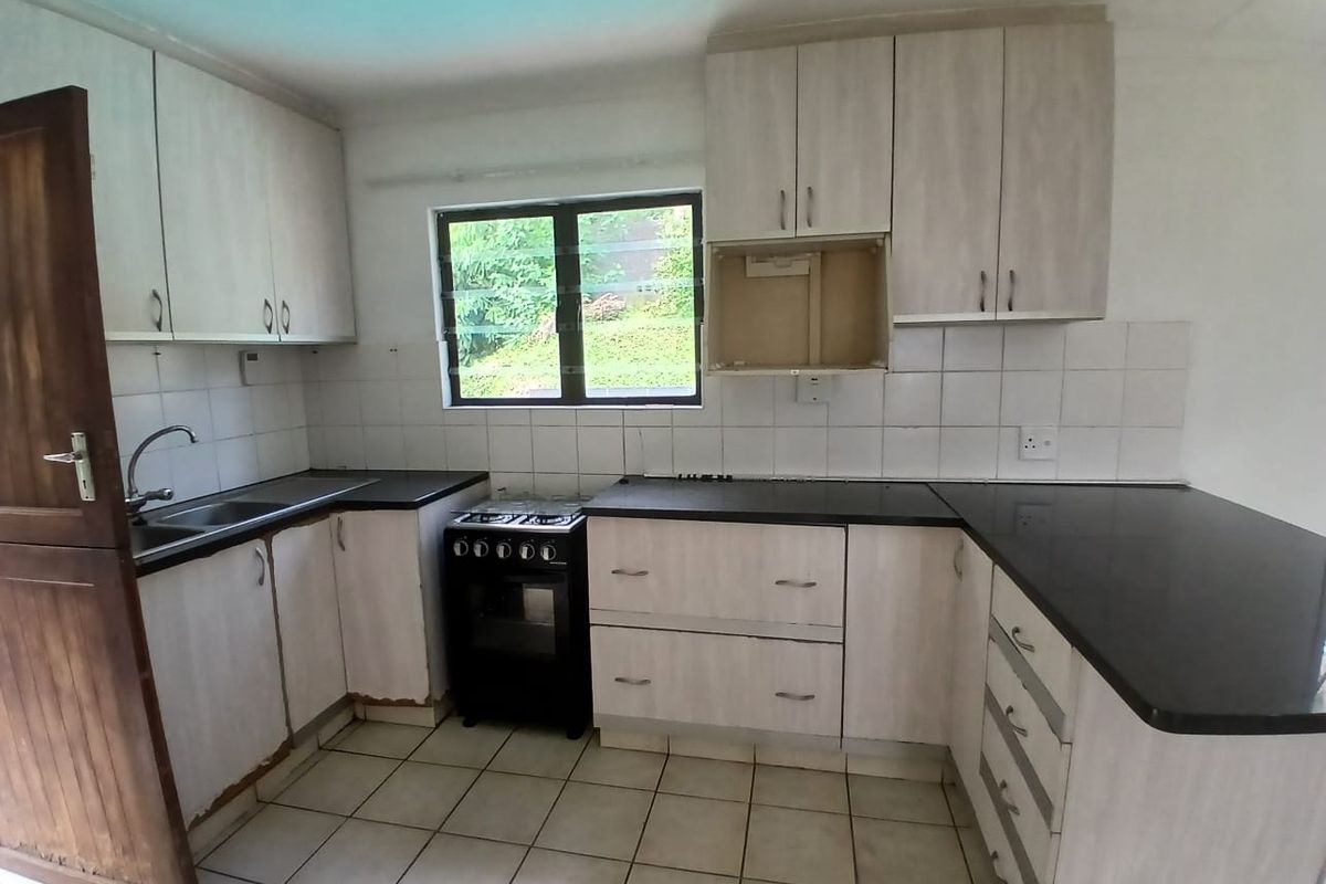 A functional kitchen featuring laminate cabinetry, black countertops, a freestanding stove, and tiled flooring, offering a blank canvas for potential cosmetic updates.