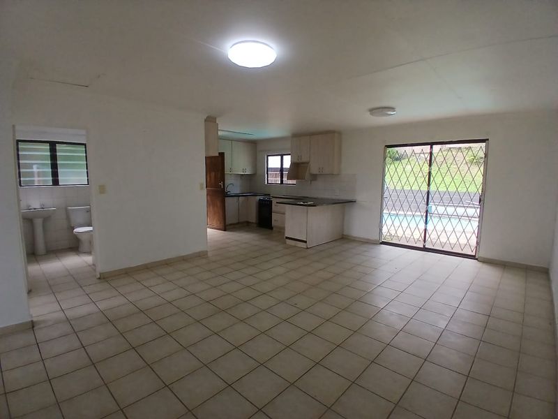 Spacious open-plan living area featuring tiled floors, a functional kitchen with built-in cabinetry, and direct access to the outdoor pool area.