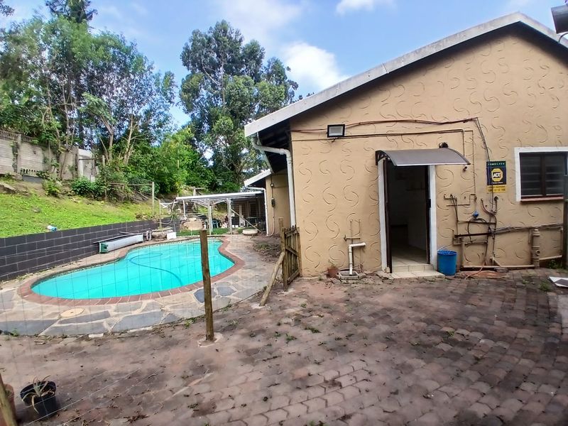 Rear exterior view of the cottage featuring a swimming pool, paved patio area, and exterior wall access with security infrastructure.