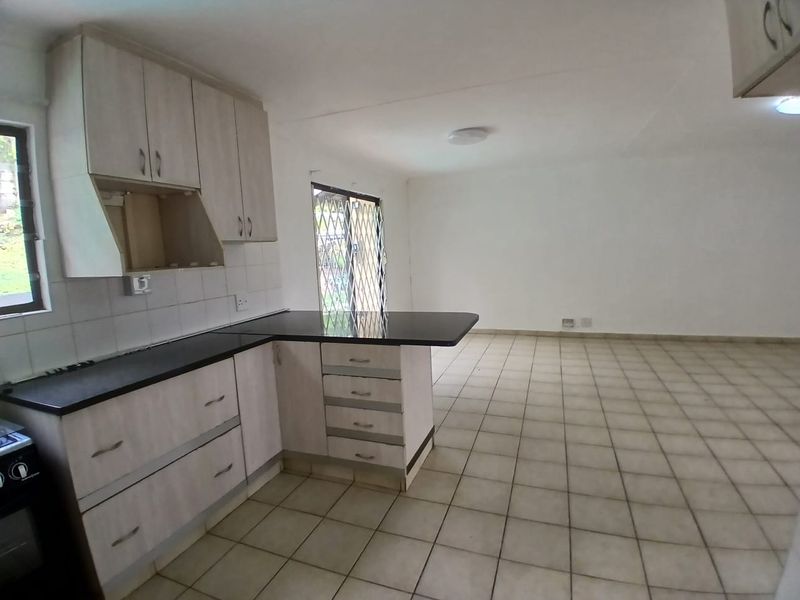 Open-plan kitchen and living area featuring light-toned cabinetry, granite countertops, tiled flooring, and direct access to the exterior via a security gate.