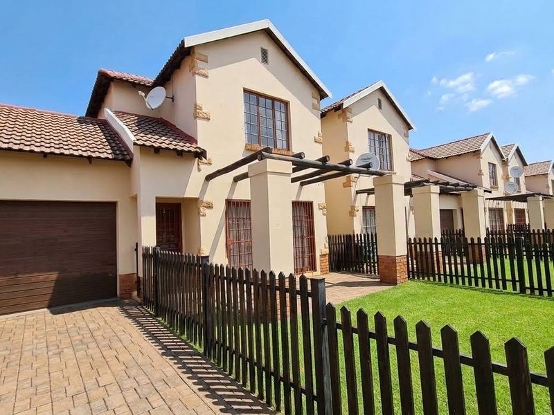 Front view of a townhouse complex featuring a brick driveway, private garage, and fenced garden area with pergola structures.