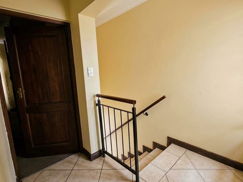 A functional hallway area featuring a staircase with a metal balustrade, wooden handrail, and tiled flooring leading to a timber door.