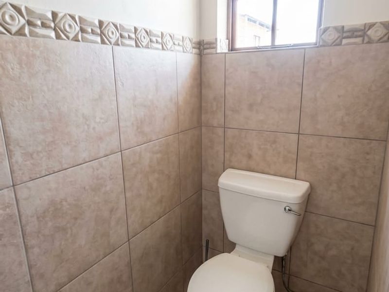 A compact guest bathroom featuring neutral ceramic wall and floor tiles with a decorative border and a standard white toilet.