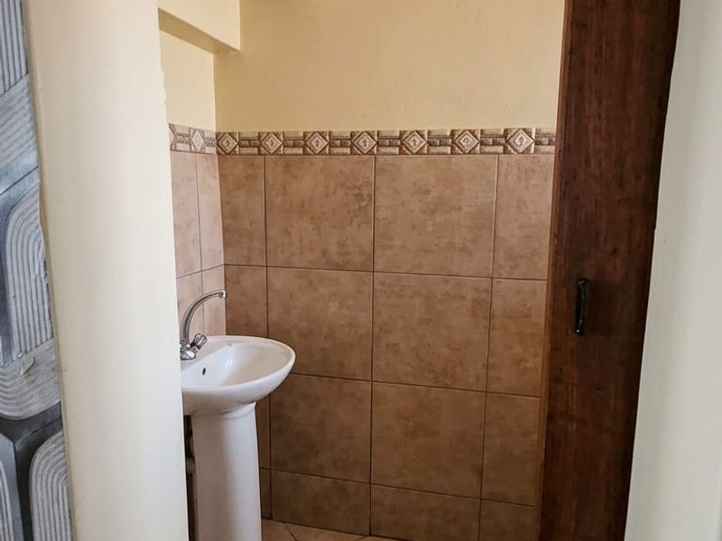 A compact guest bathroom featuring a pedestal basin, neutral ceramic wall and floor tiling, and a decorative border accent.