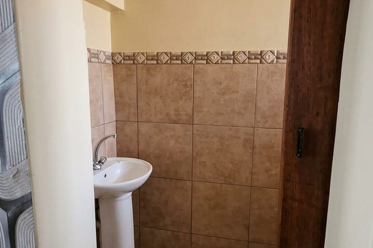 A compact guest bathroom featuring a pedestal basin, neutral ceramic wall and floor tiling, and a decorative border accent.