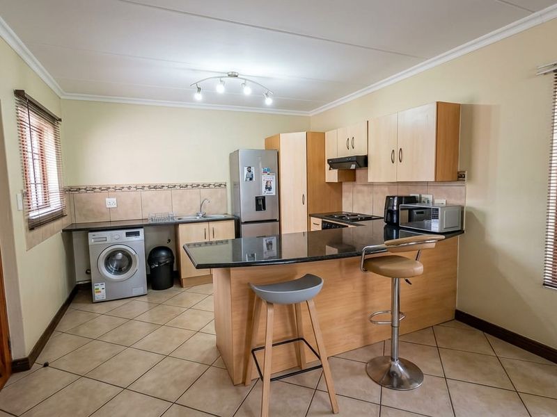 Functional kitchen featuring granite countertops, built-in cabinetry, integrated hob, extractor fan, and tiled flooring with a breakfast bar area.