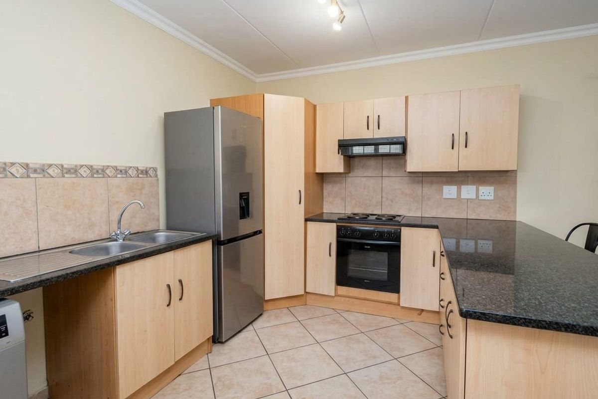 Functional kitchen featuring light wood cabinetry, granite countertops, a double sink, and built-in cooking appliances with a tiled backsplash.