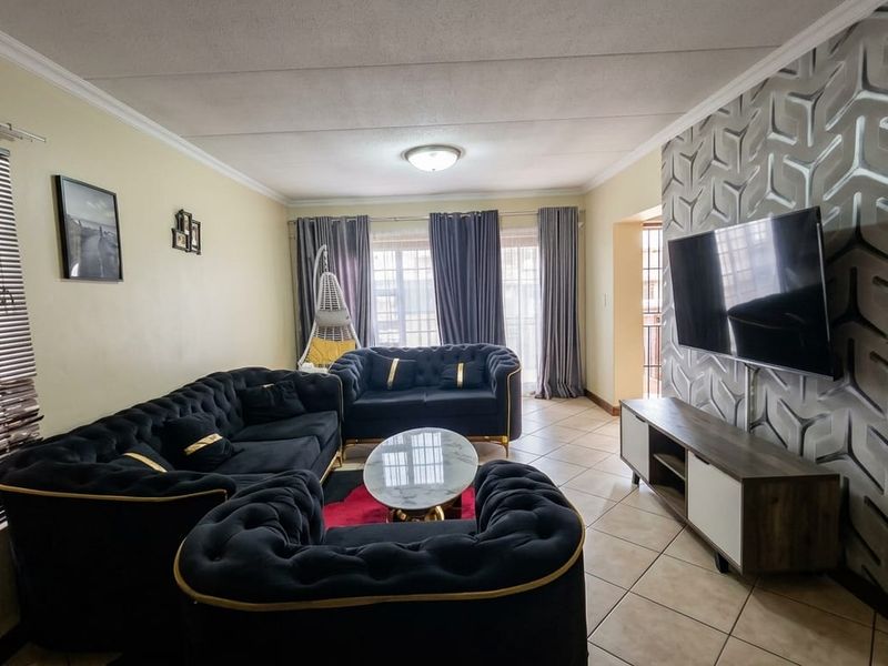 A comfortable living room featuring ceramic floor tiles, a textured feature wall, and large windows with venetian blinds, providing a functional and inviting space.