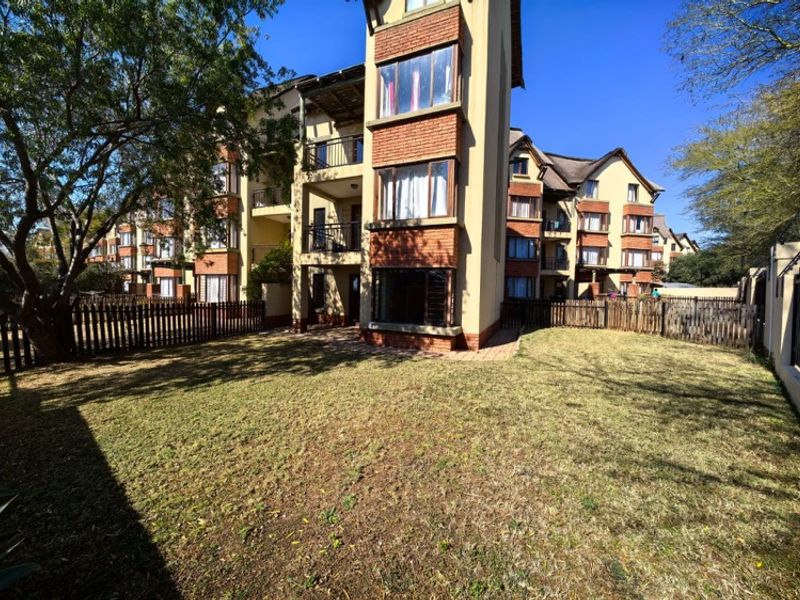 Rear view of a multi-story apartment complex featuring brick facade detailing, private balconies, and a shared garden area with timber fencing.