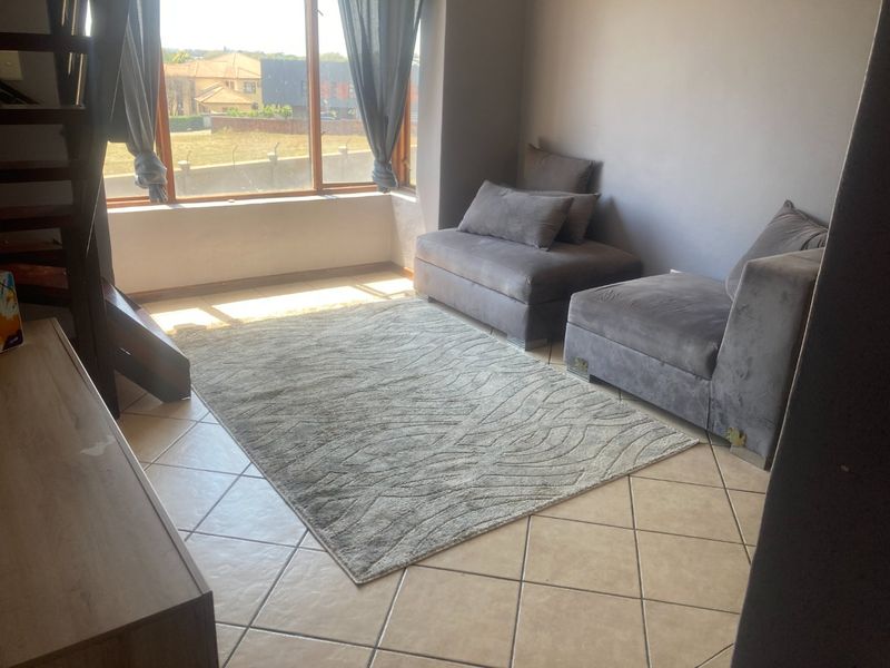 A living area featuring tiled flooring, a large window providing natural light, and an integrated staircase leading to an upper level.