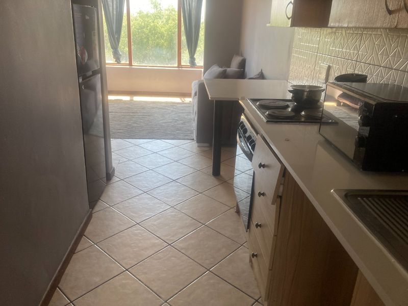 Open plan kitchen and living area featuring tiled flooring, built-in cabinetry with integrated hob and oven, and large windows providing natural light.