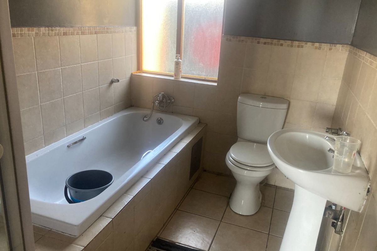 A functional bathroom featuring a built-in bathtub, pedestal basin, and toilet, finished with neutral wall and floor tiling.