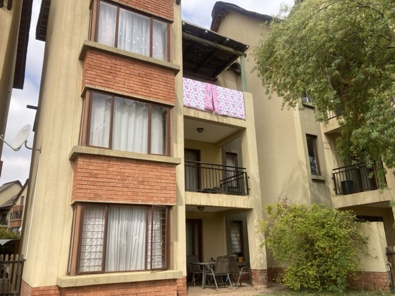 Rear elevation of a multi-story apartment building featuring brick accents, private balconies with metal railings, and security bars on windows.