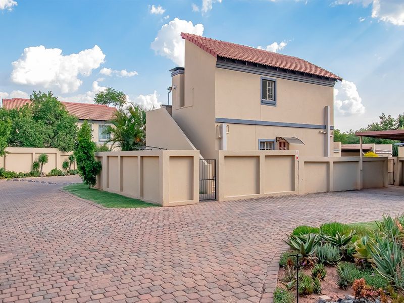 A well-maintained exterior view of an apartment unit featuring a paved driveway, perimeter wall, and a tiled roof structure.
