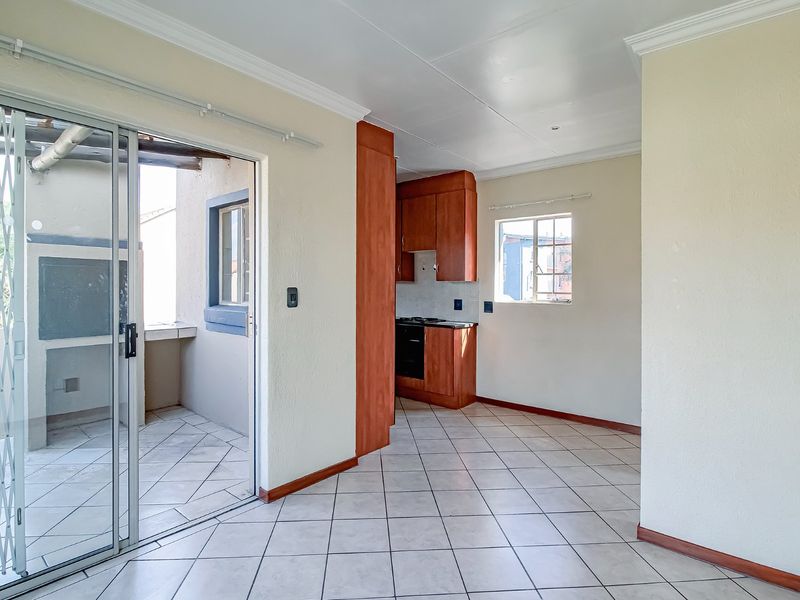 Open plan living area featuring tiled floors and a compact kitchen with built-in cabinetry, leading out to a private balcony with a built-in braai.