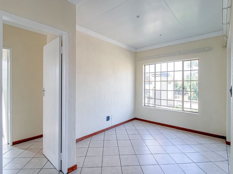 A bright, empty bedroom featuring neutral walls, tiled flooring, and a large steel-framed window providing natural light.